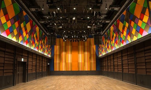 TIAT SKY HALL performance hall with colorful stained-glass-style wall panels, warm stage lighting and a wood floor